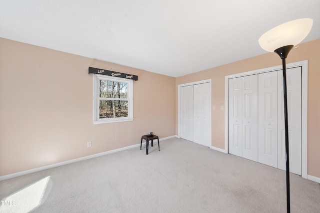 unfurnished bedroom with baseboards, carpet, and multiple closets