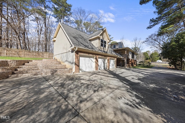 view of home's exterior with an attached garage, brick siding, a shingled roof, fence, and driveway