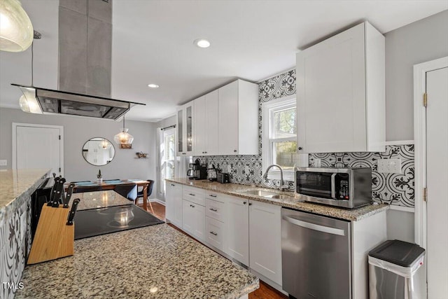 kitchen featuring decorative backsplash, appliances with stainless steel finishes, white cabinetry, a sink, and island range hood