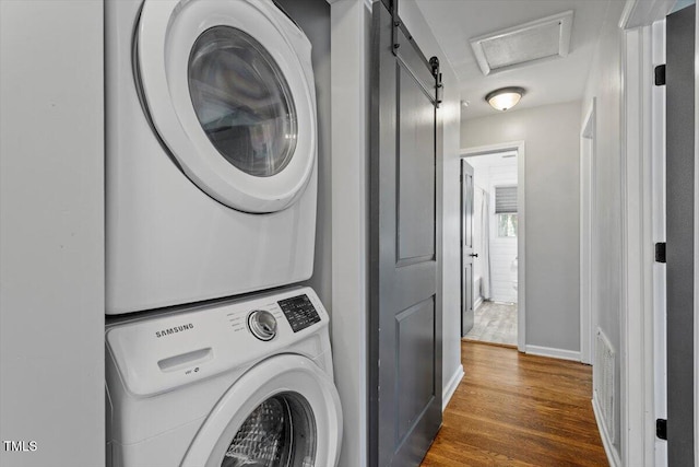 clothes washing area featuring visible vents, attic access, stacked washer / dryer, wood finished floors, and baseboards