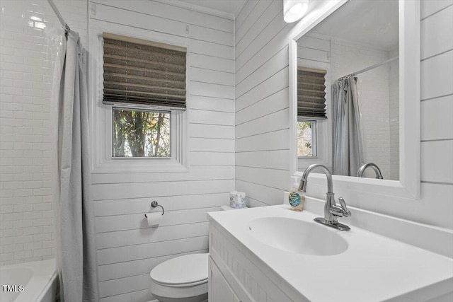 bathroom with wooden walls, vanity, toilet, and a healthy amount of sunlight