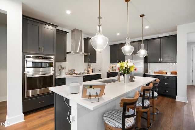 kitchen featuring a sink, appliances with stainless steel finishes, wall chimney exhaust hood, tasteful backsplash, and dark wood finished floors