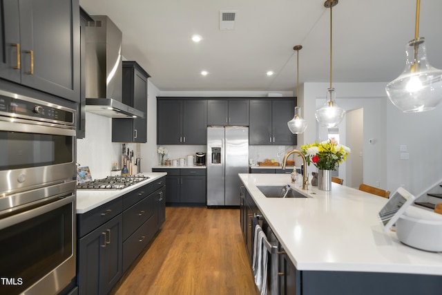 kitchen featuring a sink, visible vents, light countertops, appliances with stainless steel finishes, and wall chimney range hood