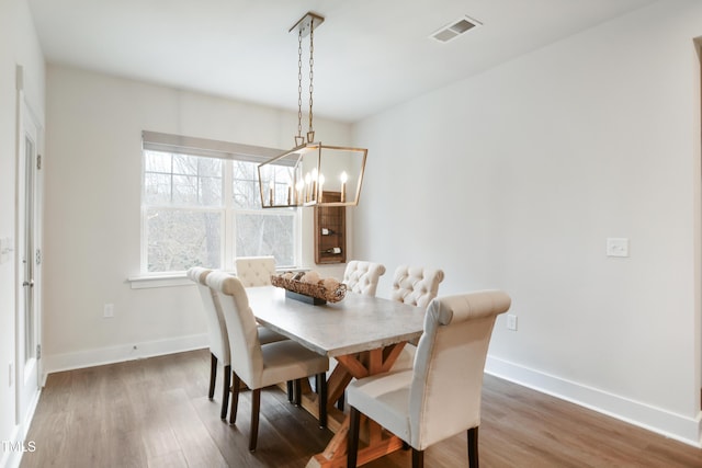 dining space featuring baseboards, visible vents, a chandelier, and wood finished floors