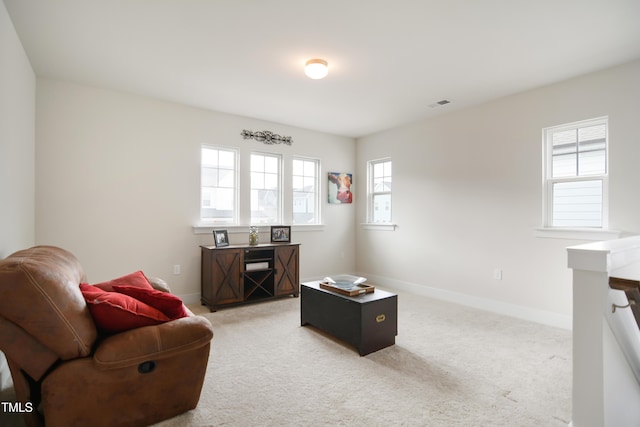 living area with baseboards, visible vents, and light colored carpet