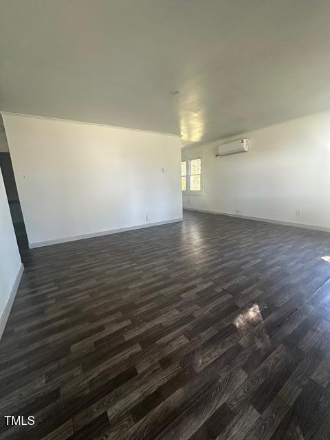 empty room with baseboards, a wall mounted air conditioner, and dark wood-type flooring