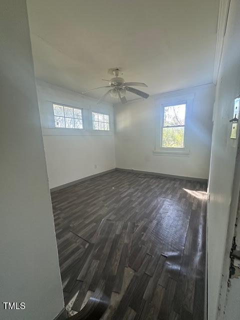 empty room featuring ceiling fan, a healthy amount of sunlight, and dark wood-type flooring