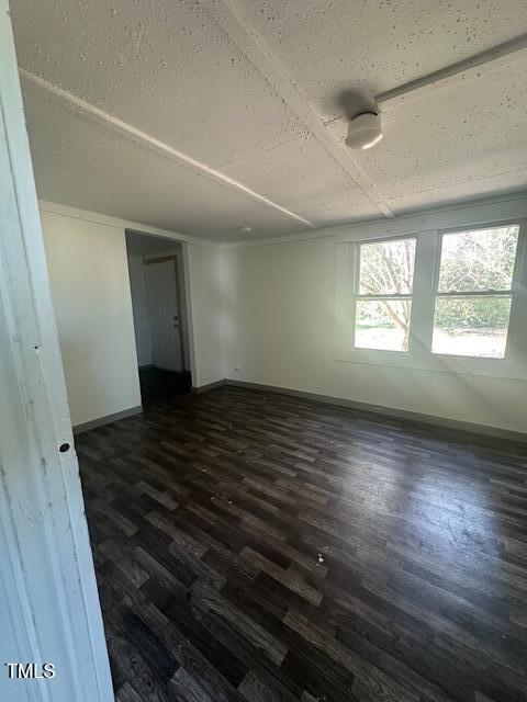 empty room with dark wood-style flooring, baseboards, and a textured ceiling