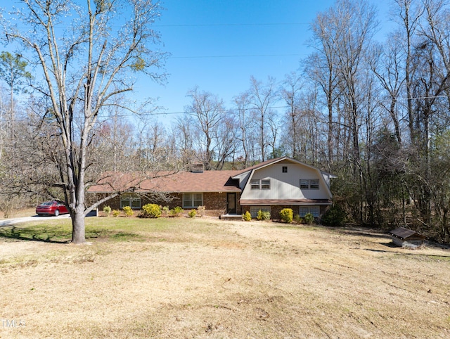 view of front of home featuring brick siding, a gambrel roof, a front lawn, and roof with shingles