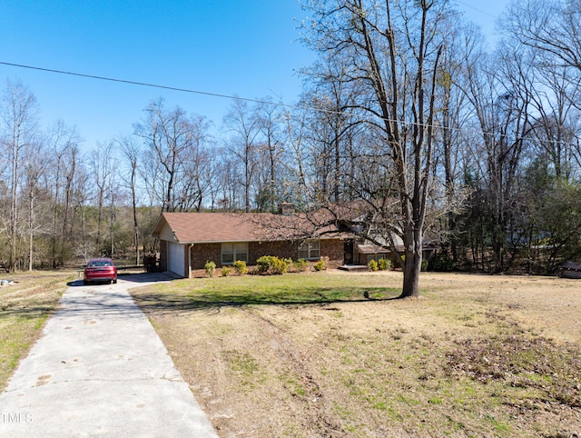 view of front facade with a front yard, driveway, an attached garage, a chimney, and brick siding