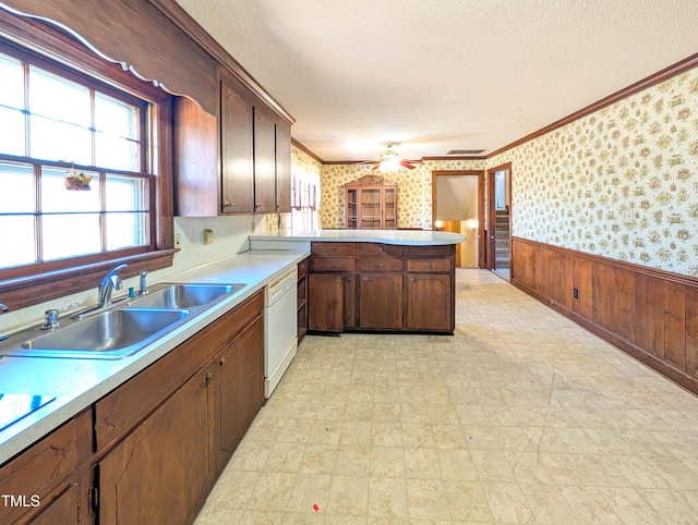 kitchen with wallpapered walls, wainscoting, white dishwasher, a textured ceiling, and a sink