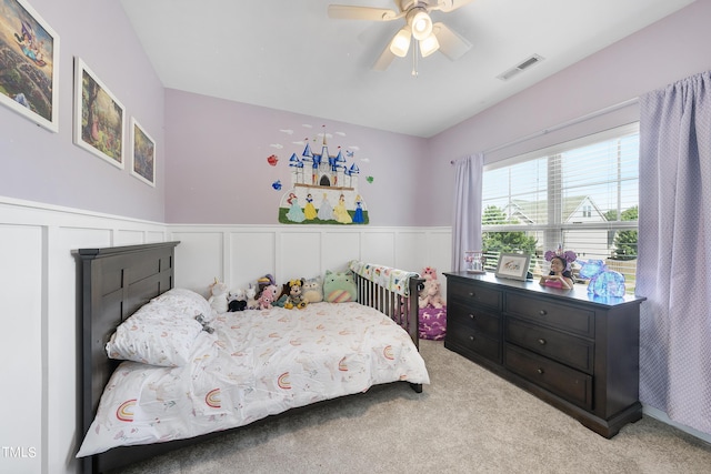 carpeted bedroom with a ceiling fan, wainscoting, and visible vents