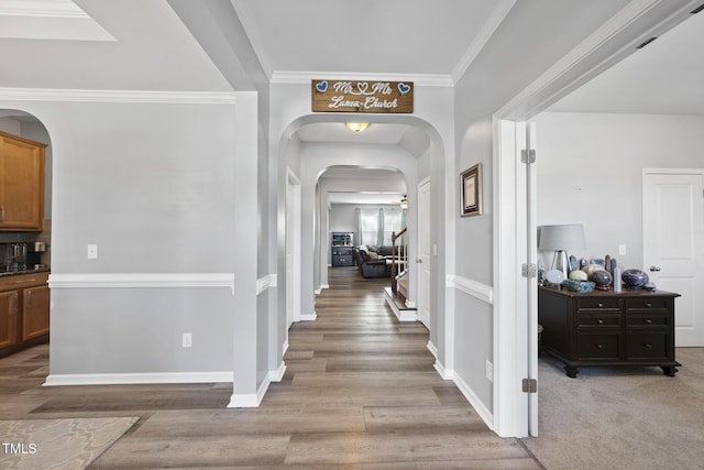 hall with light wood-style floors, arched walkways, crown molding, and baseboards