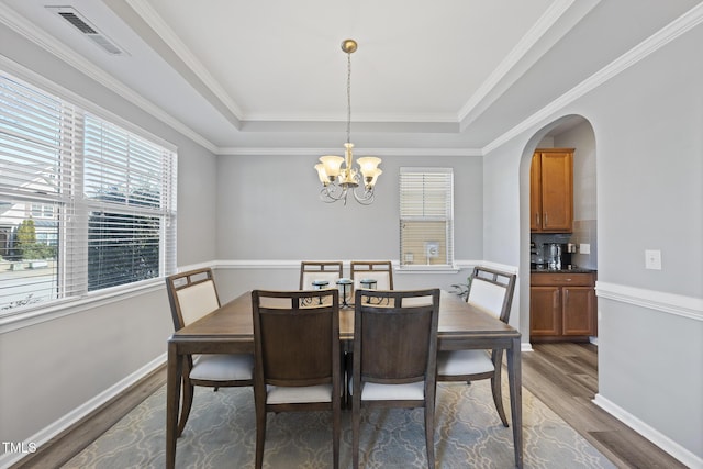 dining space with an inviting chandelier, visible vents, a tray ceiling, and wood finished floors