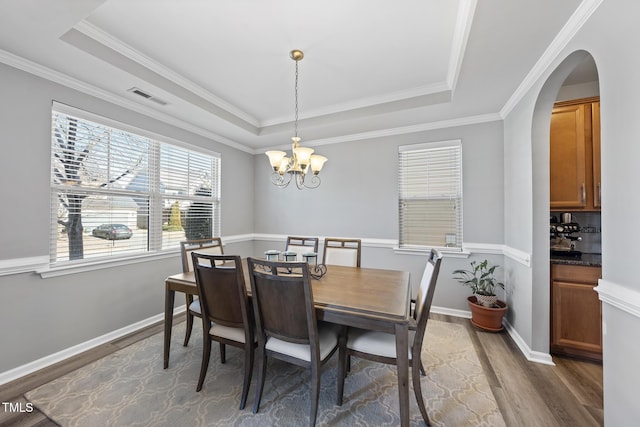 dining area with a chandelier, wood finished floors, visible vents, baseboards, and a raised ceiling