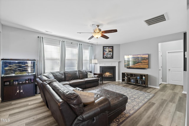 living area with a ceiling fan, a glass covered fireplace, visible vents, and light wood finished floors