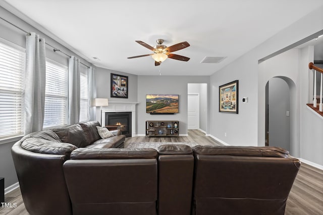 living room with arched walkways, ceiling fan, wood finished floors, visible vents, and a glass covered fireplace