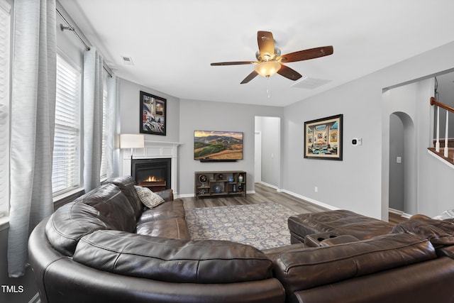 living room featuring visible vents, arched walkways, a ceiling fan, a glass covered fireplace, and wood finished floors