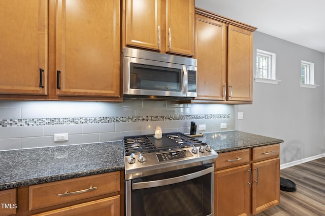 kitchen featuring stainless steel appliances, wood finished floors, baseboards, backsplash, and dark stone counters