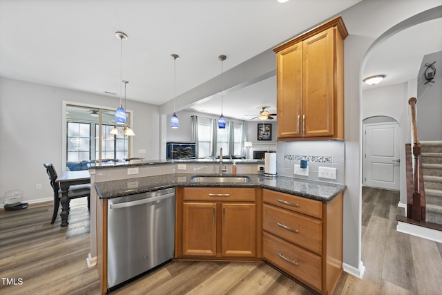 kitchen with a sink, brown cabinetry, dark stone counters, and stainless steel dishwasher