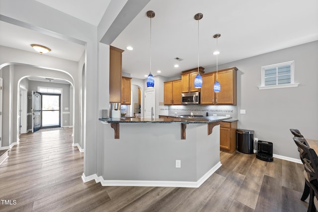 kitchen with a kitchen bar, stainless steel microwave, arched walkways, and wood finished floors