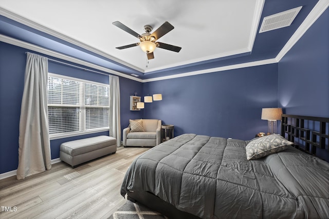 bedroom with visible vents, a ceiling fan, ornamental molding, wood finished floors, and a tray ceiling