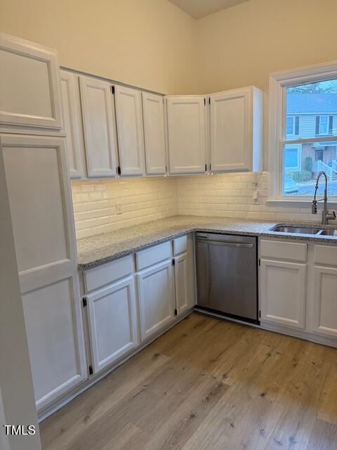 kitchen featuring a sink, decorative backsplash, stainless steel dishwasher, and white cabinetry