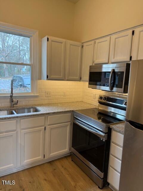 kitchen with tasteful backsplash, white cabinets, appliances with stainless steel finishes, and a sink