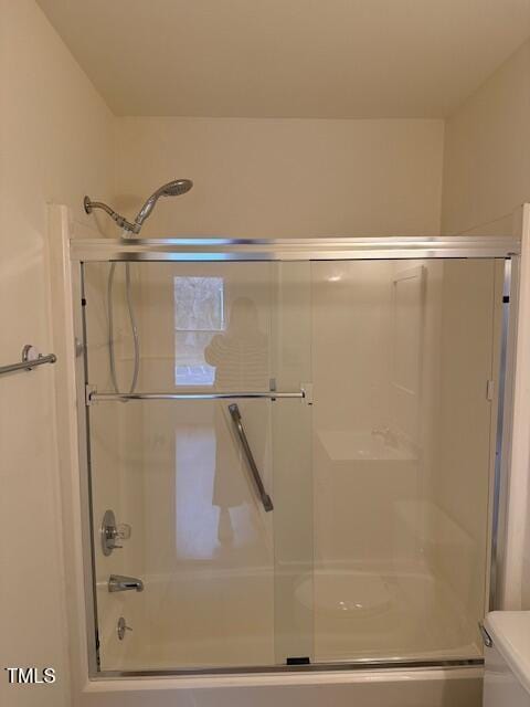 full bath featuring combined bath / shower with glass door and toilet