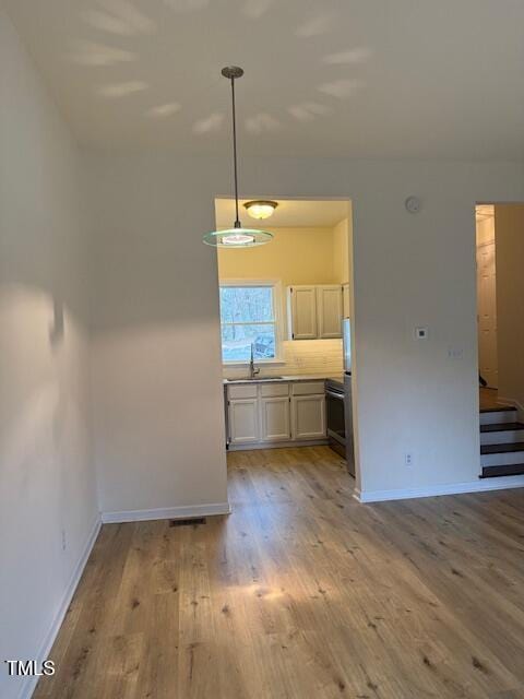 unfurnished dining area featuring stairs, baseboards, light wood finished floors, and a sink