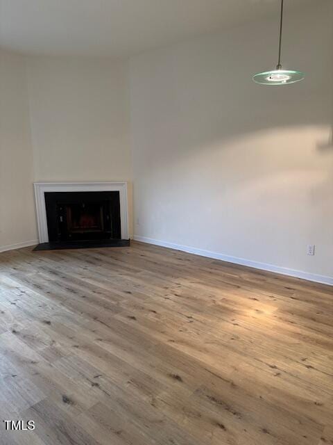 unfurnished living room featuring a fireplace with flush hearth, baseboards, and wood finished floors