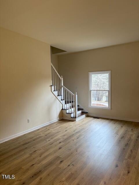 spare room with stairs, wood finished floors, and baseboards