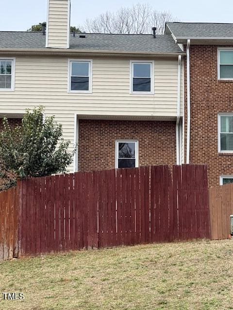 view of home's exterior with a lawn, fence, a shingled roof, brick siding, and a chimney