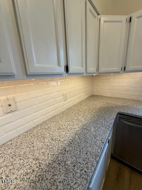 interior details with dishwashing machine, white cabinets, light stone counters, and backsplash