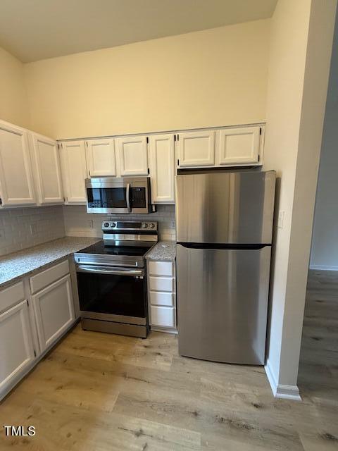 kitchen with backsplash, light wood-type flooring, light countertops, stainless steel appliances, and white cabinetry