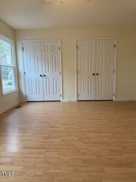 unfurnished bedroom featuring baseboards, visible vents, two closets, and light wood-style floors