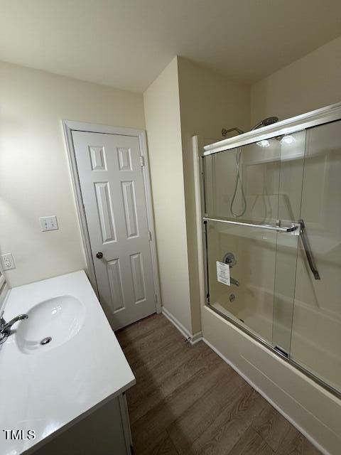 bathroom featuring bath / shower combo with glass door, wood finished floors, and vanity