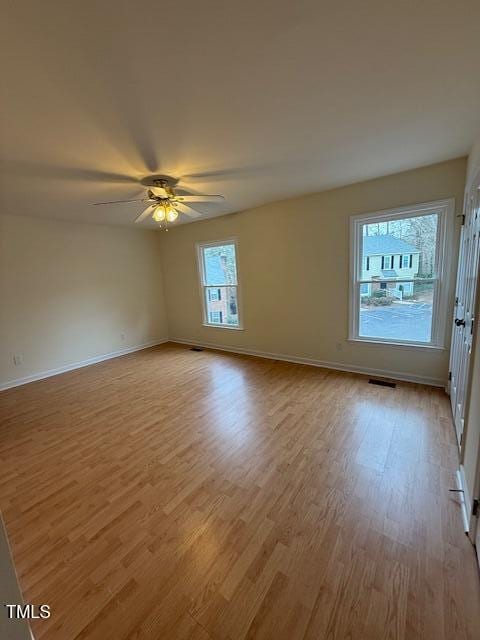 empty room featuring ceiling fan, visible vents, baseboards, and wood finished floors