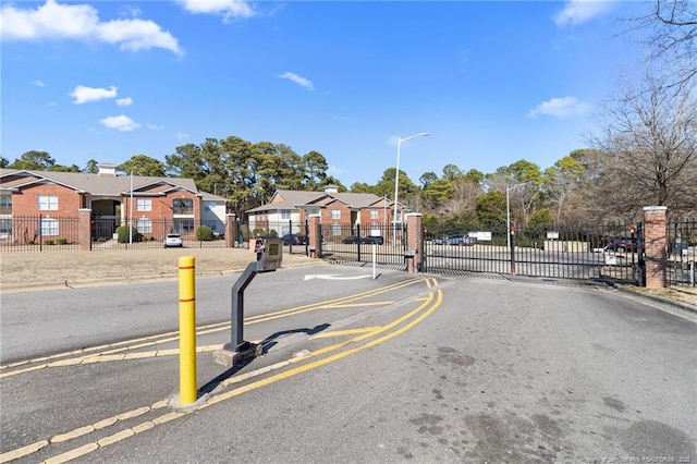 view of road with curbs, street lighting, a gated entry, and a residential view