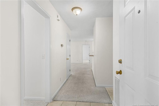 hallway featuring light carpet, light tile patterned floors, visible vents, and baseboards