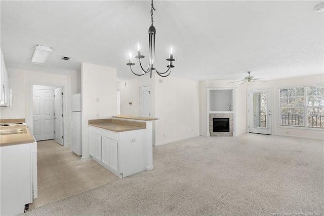 kitchen with freestanding refrigerator, a tiled fireplace, white cabinets, and light colored carpet