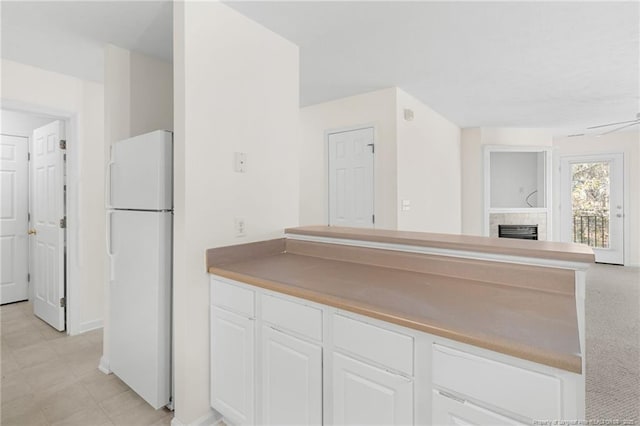 kitchen with freestanding refrigerator, white cabinets, a fireplace, and ceiling fan