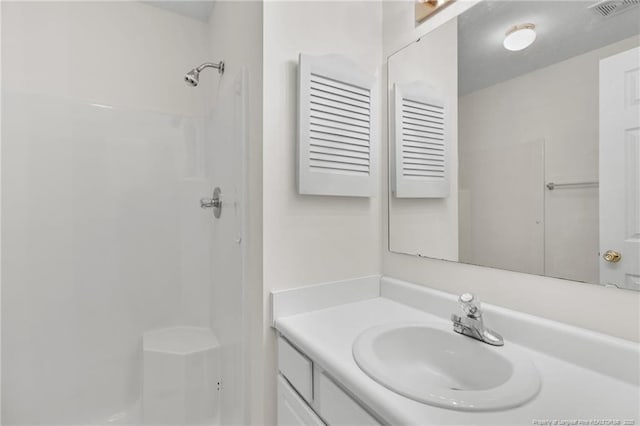 bathroom with visible vents, walk in shower, and vanity