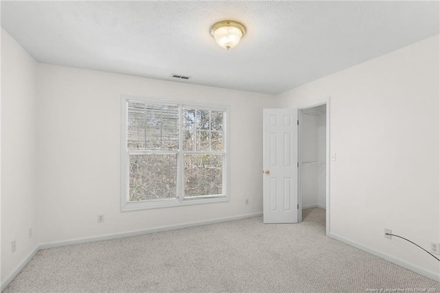 unfurnished bedroom featuring baseboards, visible vents, a spacious closet, a textured ceiling, and carpet flooring