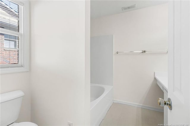 full bathroom with toilet, a tub to relax in, visible vents, and baseboards