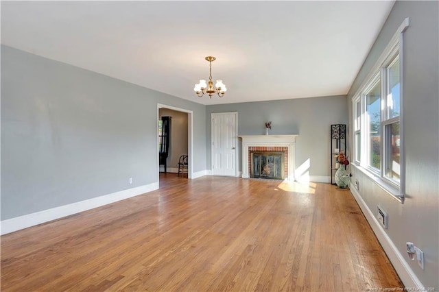 unfurnished living room with a fireplace, visible vents, an inviting chandelier, light wood-type flooring, and baseboards