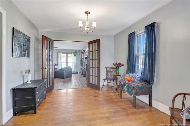 interior space with french doors, baseboards, a notable chandelier, and light wood finished floors