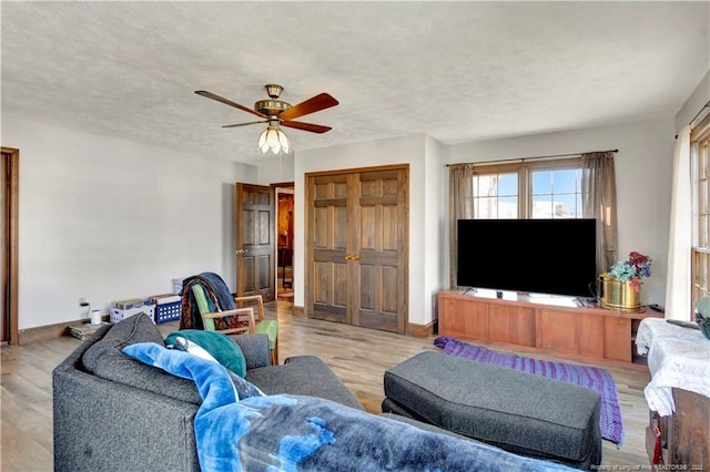 living room with ceiling fan, a textured ceiling, baseboards, and wood finished floors