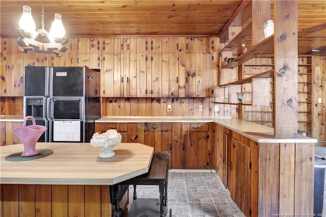 kitchen featuring brown cabinets, light countertops, black fridge with ice dispenser, wooden walls, and wooden ceiling