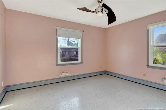 unfurnished room with a baseboard heating unit, plenty of natural light, a ceiling fan, and wood finished floors